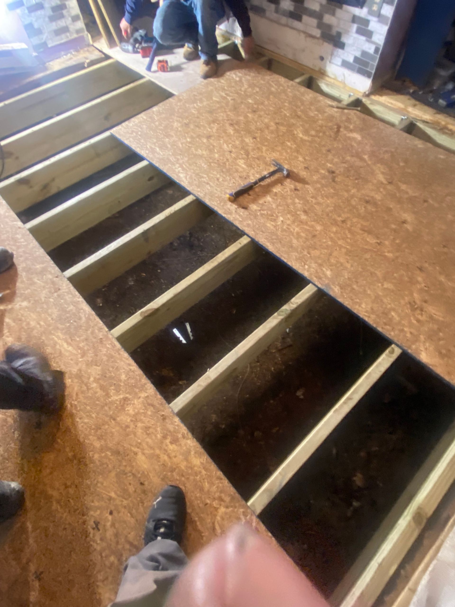 Construction: Installing OSB subflooring over joists. Workers in background.