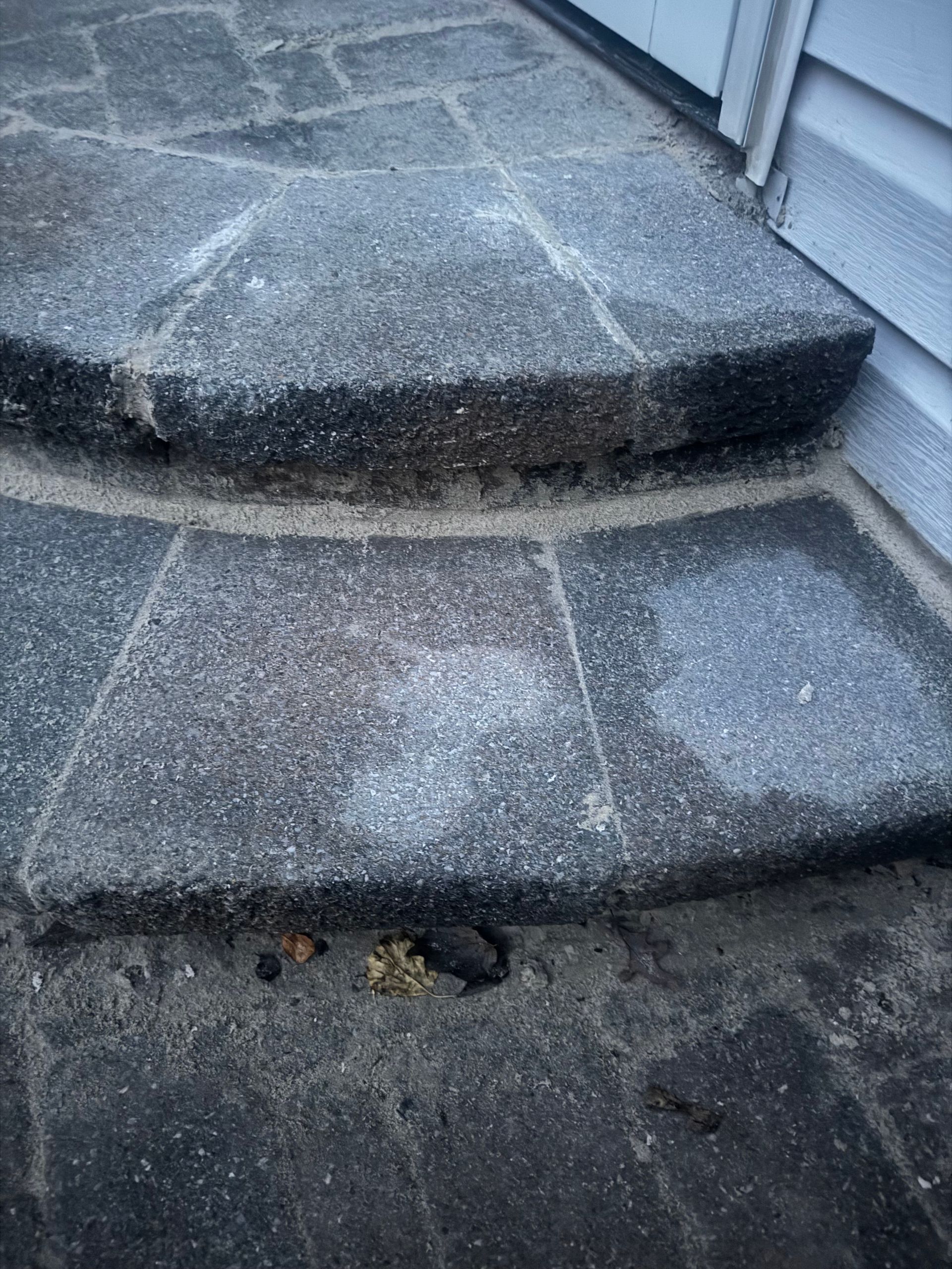 Concrete steps leading to a building's entrance. The steps have a rounded edge and are weathered.
