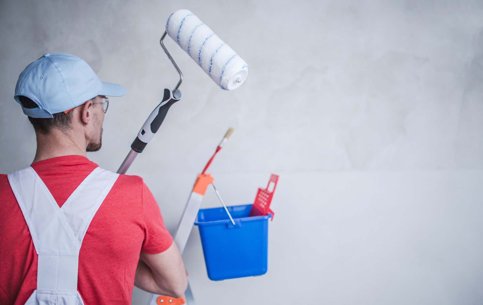 A man is painting a wall with a paint roller and bucket.