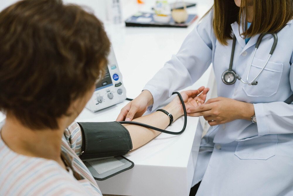 A Doctor Checks a Patient's Blood Pressure Using a Digital Monitor and Arm Cuff While Holding the Patient's Wrist in A Clinical Setting — Tuncurry Medical Centre In Tuncurry, NSW