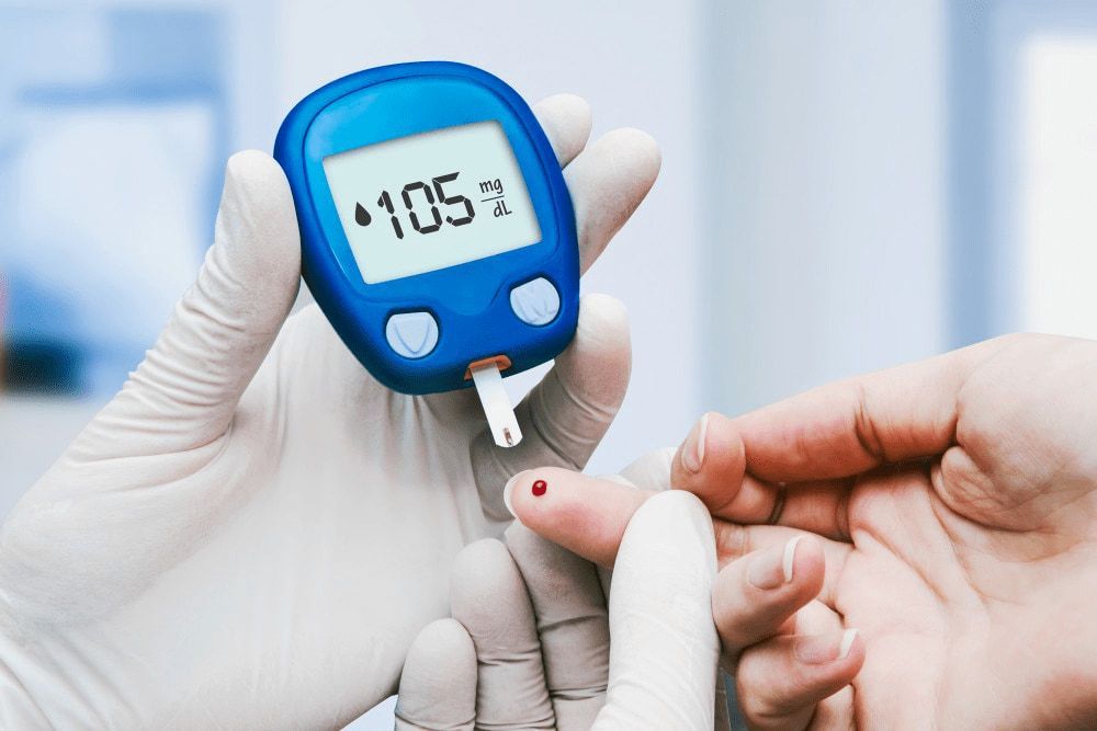 A healthcare worker wearing gloves checks a patient's blood sugar level using a glucose meter, which displays a reading of 105 mg/dL — Tuncurry Medical Centre In Tuncurry, NSW