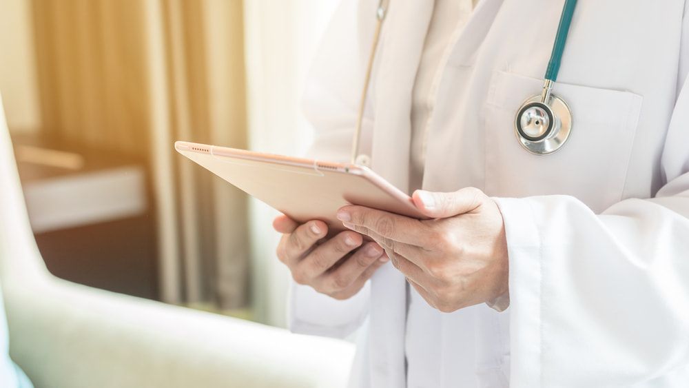 A Doctor Is Holding a Tablet in His Hands in A Hospital Room — Tuncurry Medical Centre In Tuncurry, NSW