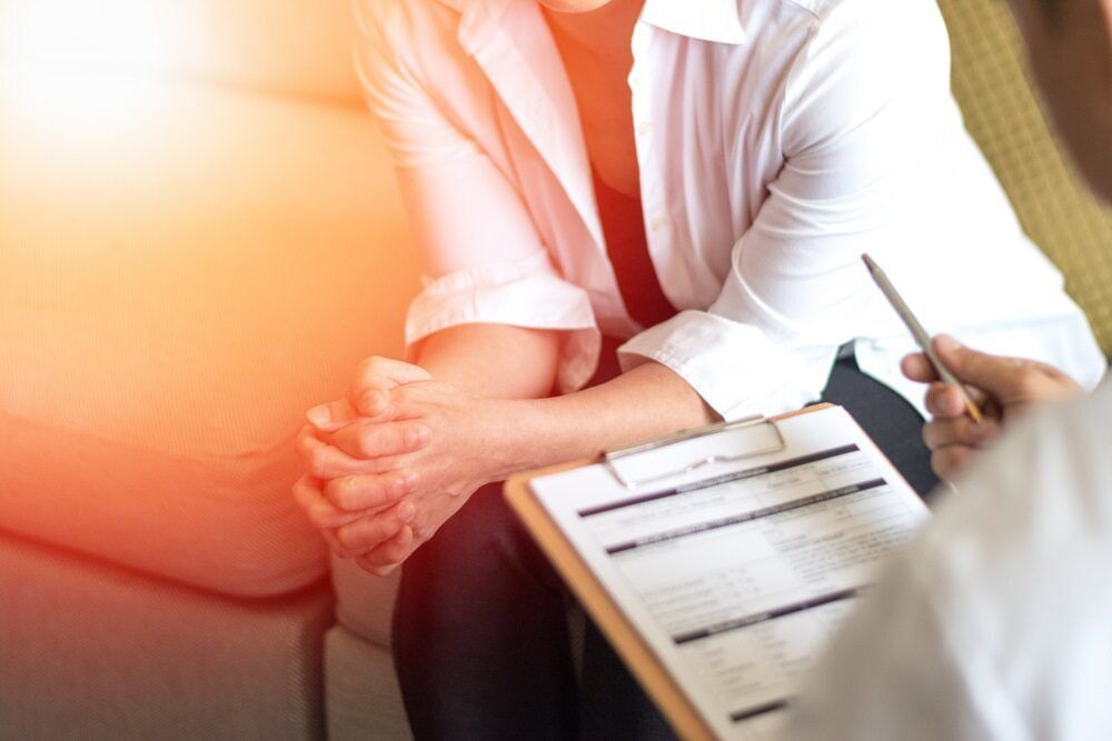 A Woman Is Sitting on A Couch Talking to A Doctor While Holding a Clipboard — Tuncurry Medical Centre In Tuncurry, NSW