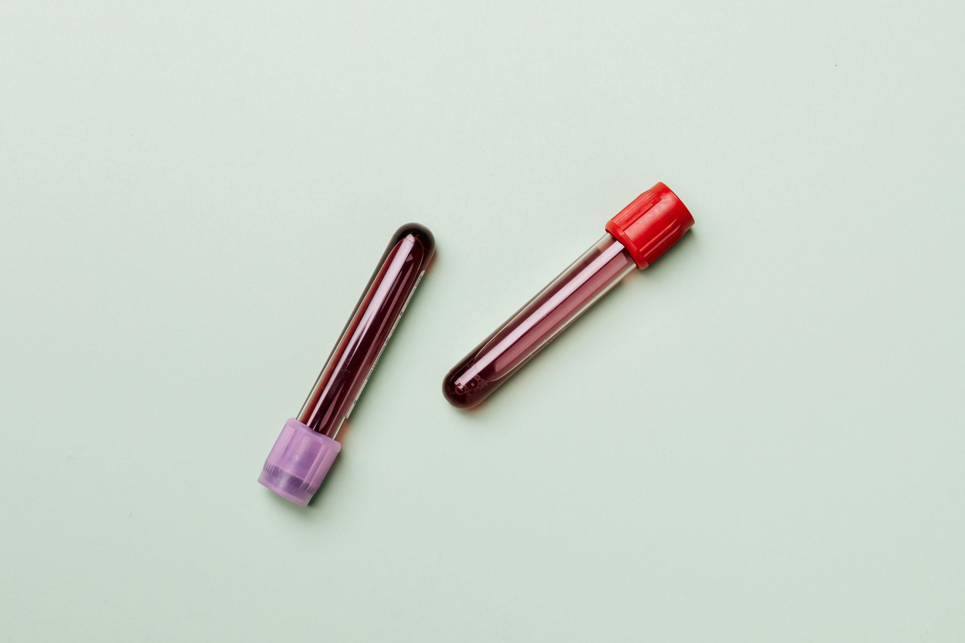 Two blood sample tubes, one with a purple cap and one with a red cap, on a pale green surface - Tuncurry Medical Centre In Tuncurry, NSW