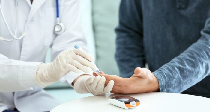 A Healthcare Professional Wearing Gloves Pricks a Patient’s Finger to Collect a Blood Sample for Glucose Testing, with A Blood Glucose Meter Placed on The Table — Tuncurry Medical Centre In Tuncurry, NSW