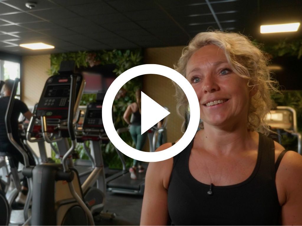 Een vrouw staat voor een afspeelknop in een sportschool.