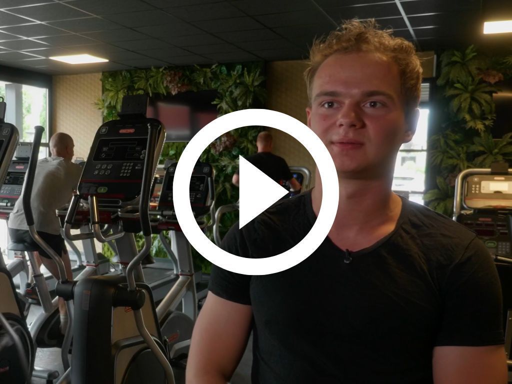 Een vrouw staat voor een afspeelknop in een sportschool.