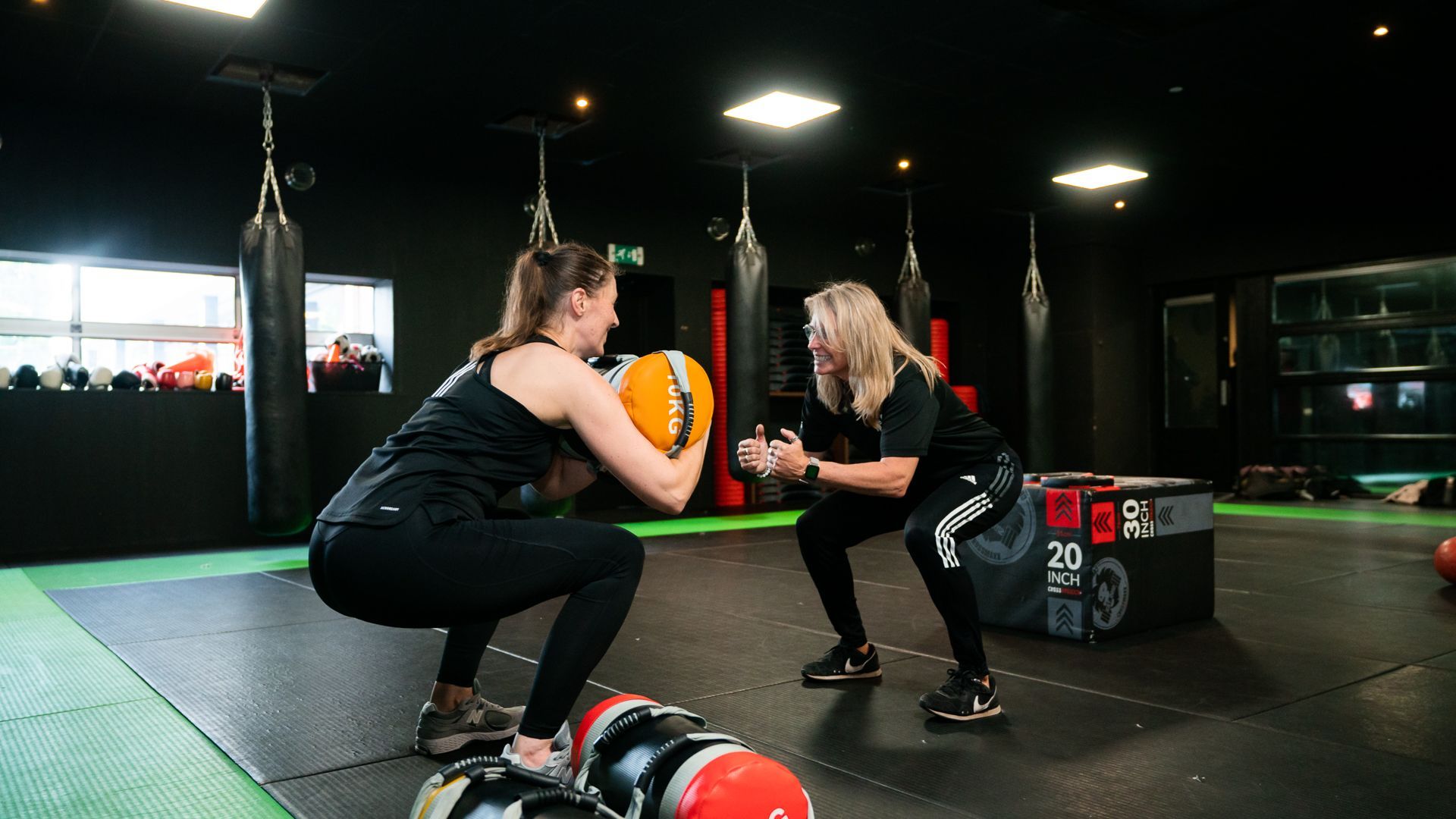 Twee vrouwen hurken met halters in een sportschool.