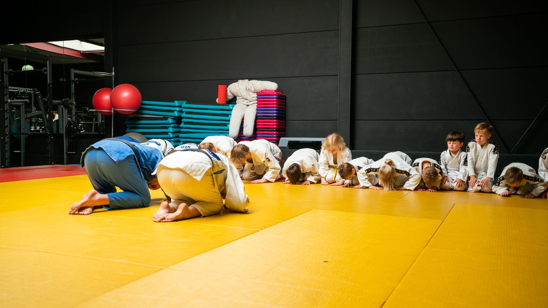 Een groep judoka's zit op de grond in een gymzaal.