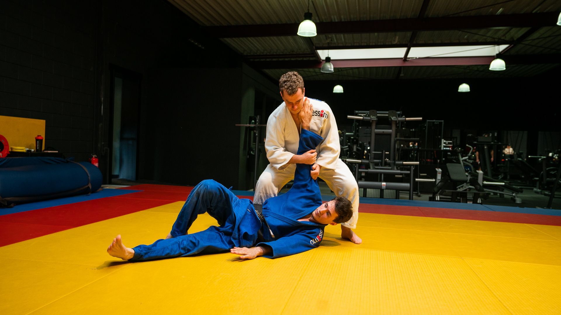 Twee mannen beoefenen judo op een mat in een gymzaal.