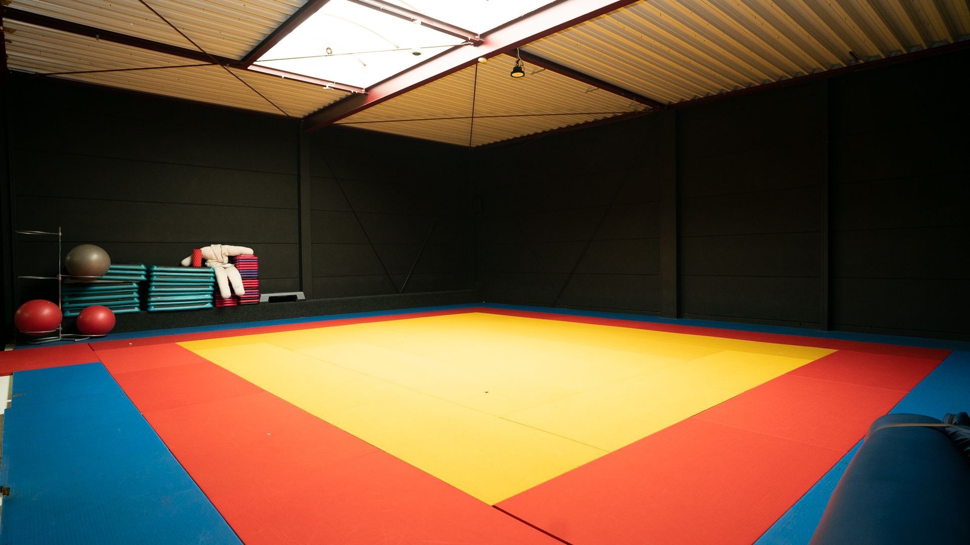 Een lege gymzaal met een rode, gele en blauwe mat.