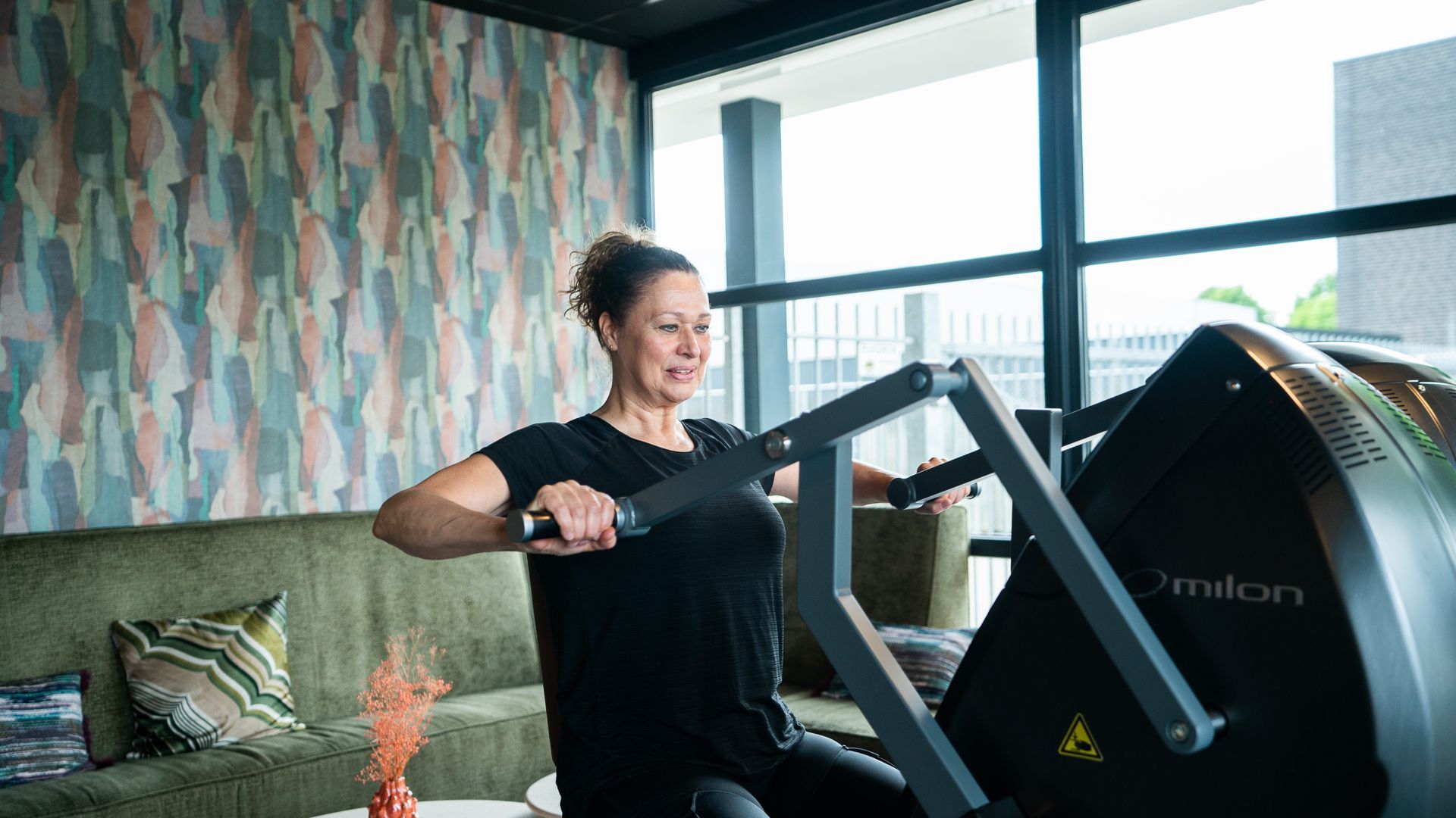 Een vrouw zit in de woonkamer op een roeimachine.
