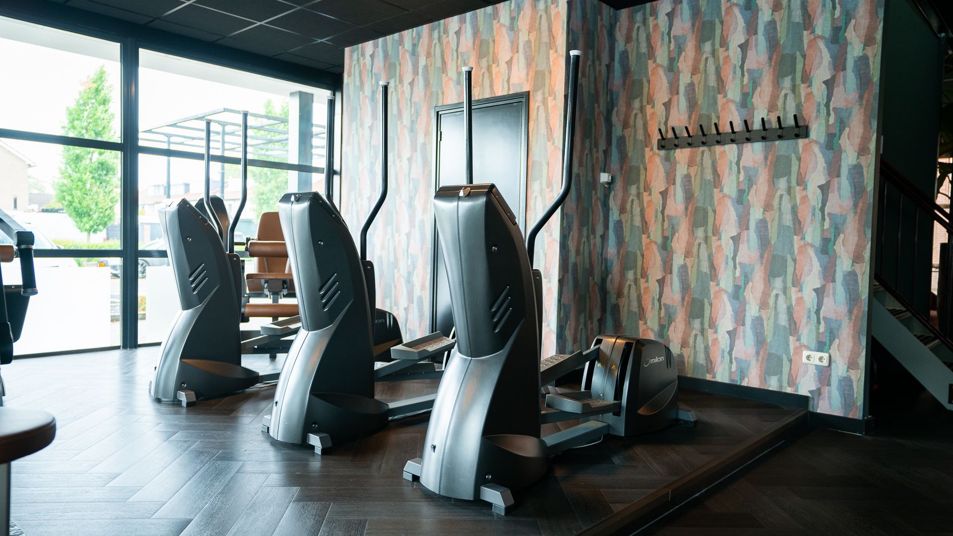 Een sportschool met veel fitnessapparatuur en een groot raam.