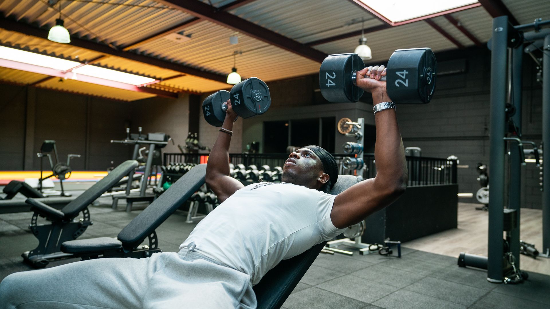 Een man tilt halters op een bankje in een sportschool.