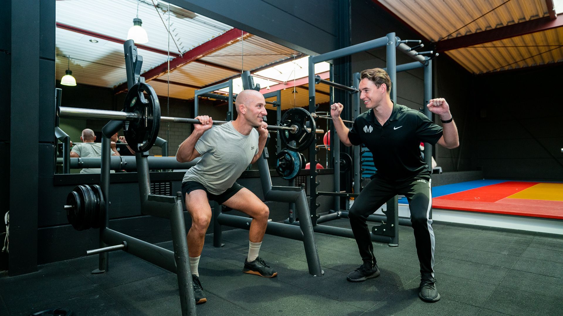 Twee mannen hurken met een halter in een sportschool.