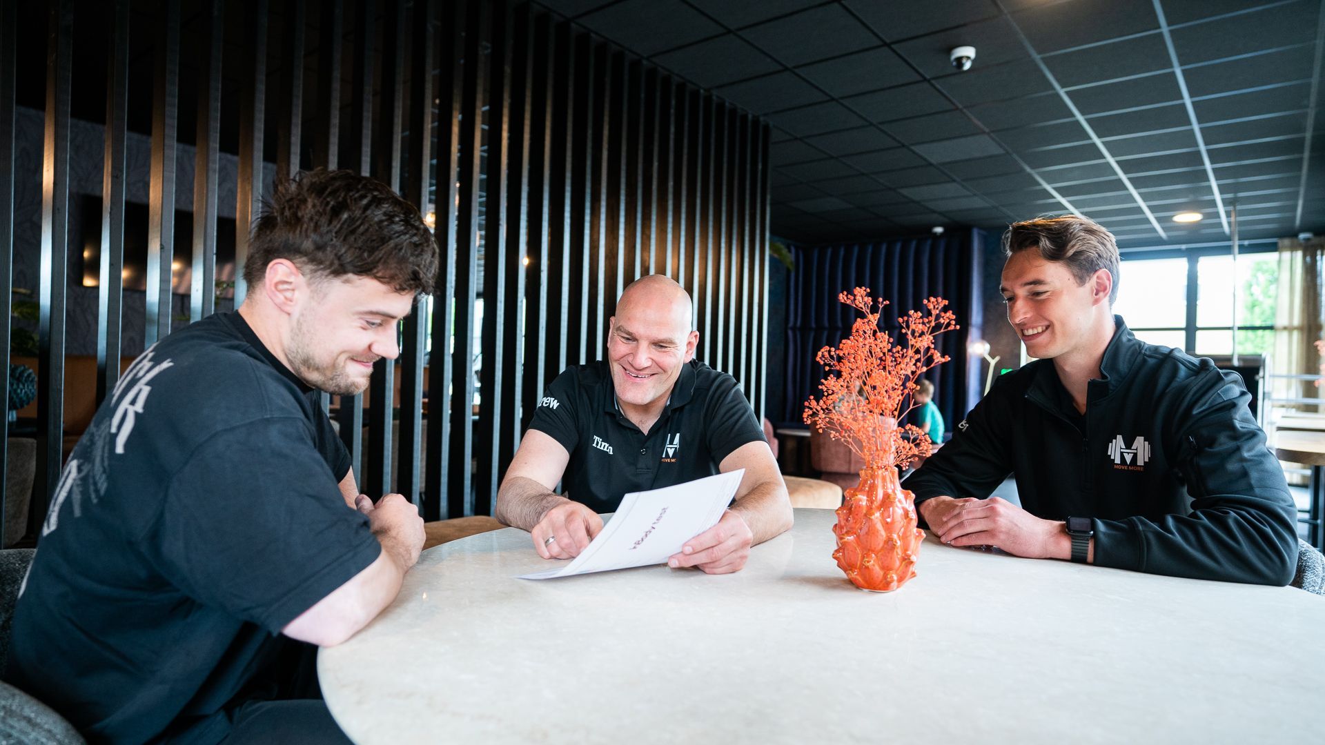 Drie mannen zitten aan een tafel en kijken naar een stuk papier.