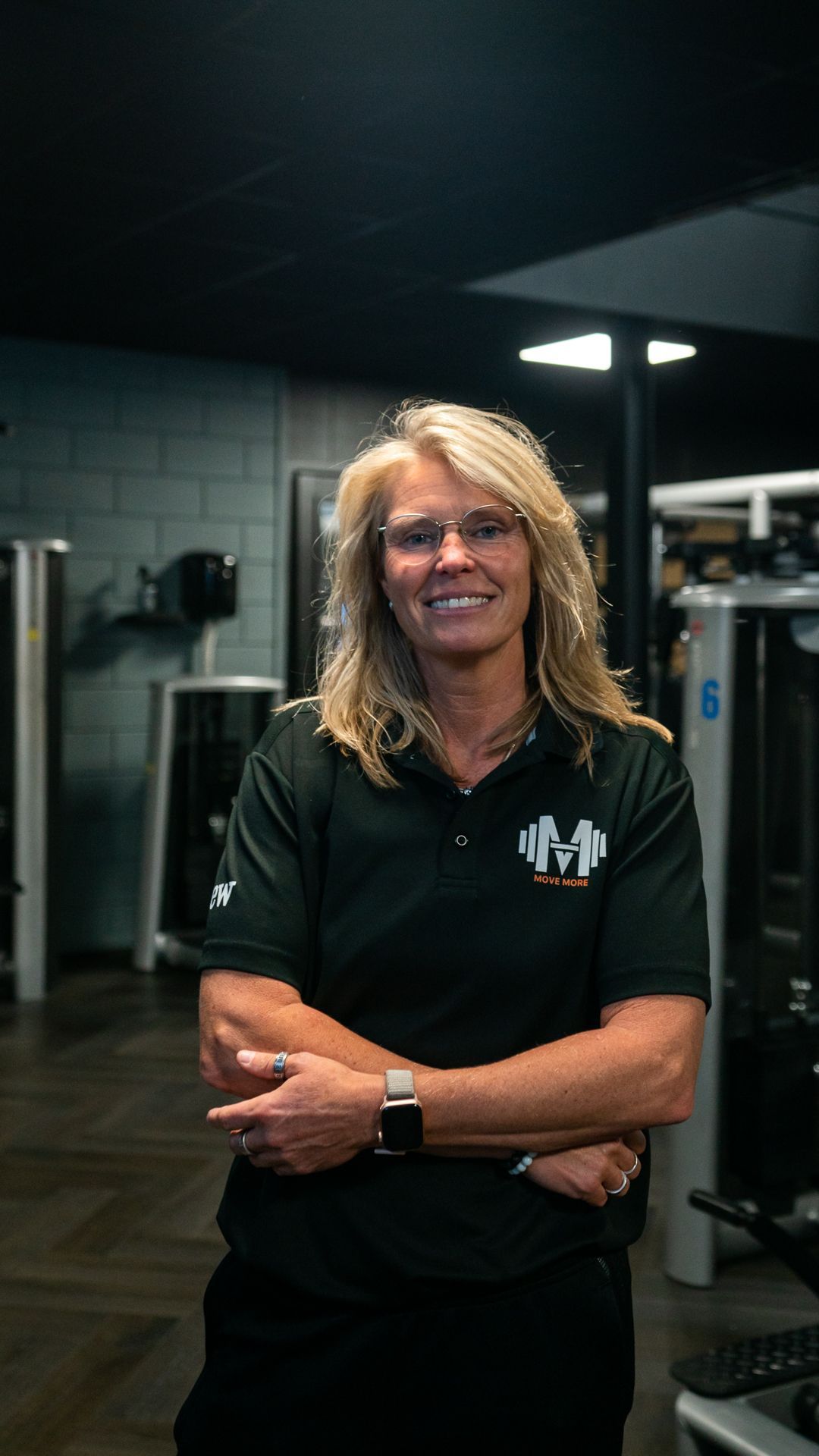 Een man in een zwart shirt staat in een sportschool met zijn armen over elkaar.