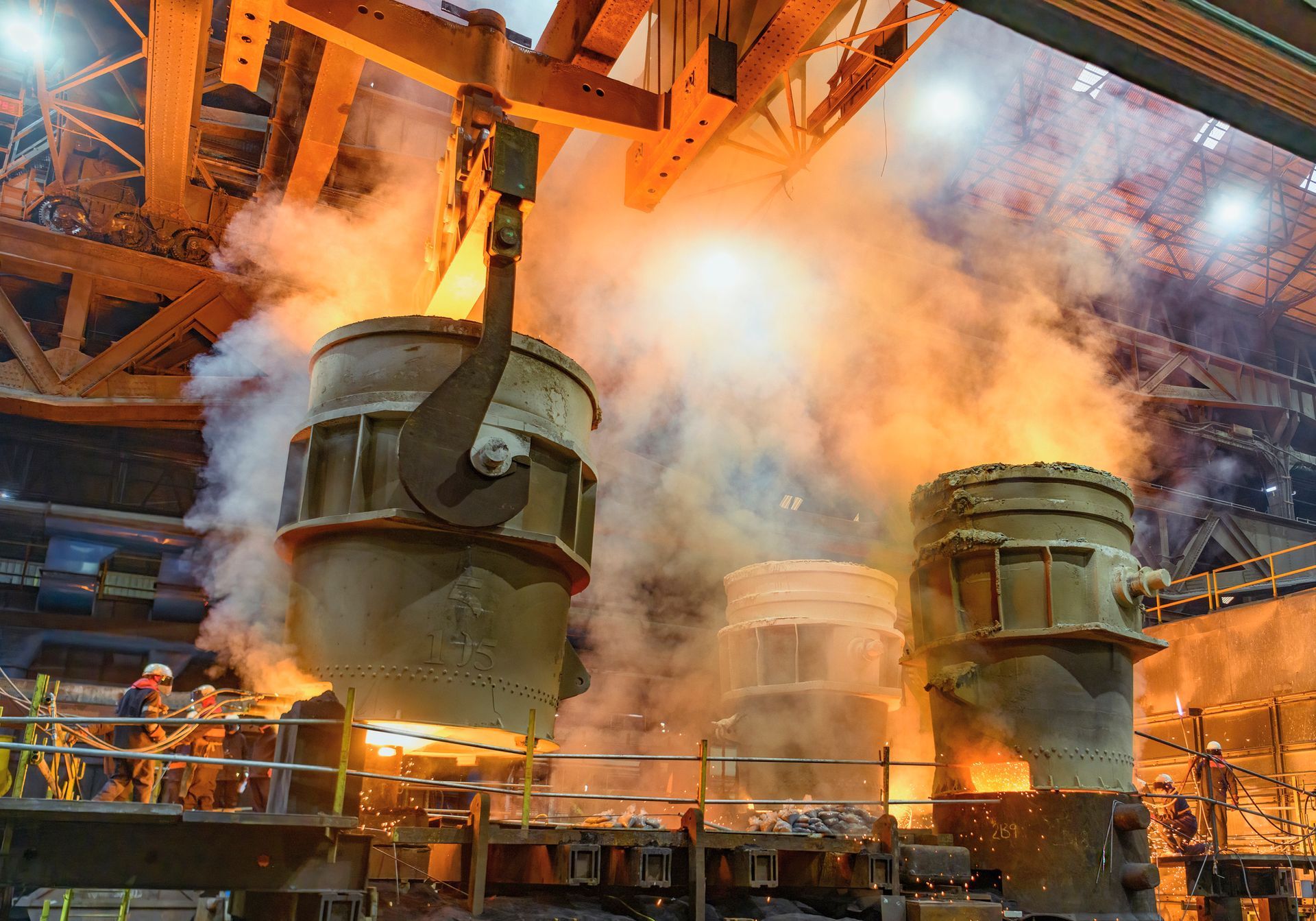 Three flasks pouring molten steel into moulds with steelworkers in steelworks.