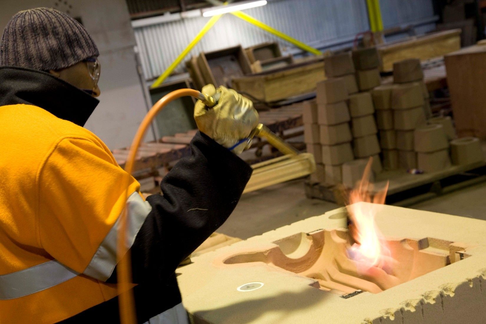 Person in safety gear using a torch to heat metal inside a mold in a workshop. Person in safety gear using a torch to heat metal inside a mold in a workshop.