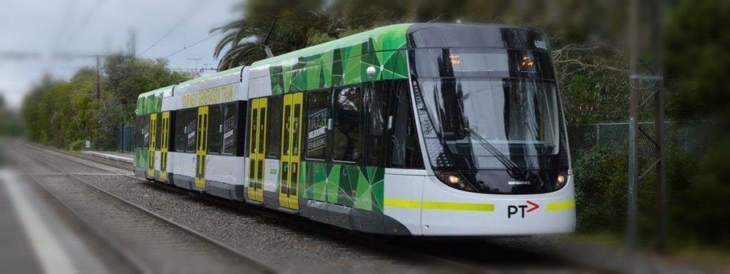 A green and yellow train is going down the tracks.