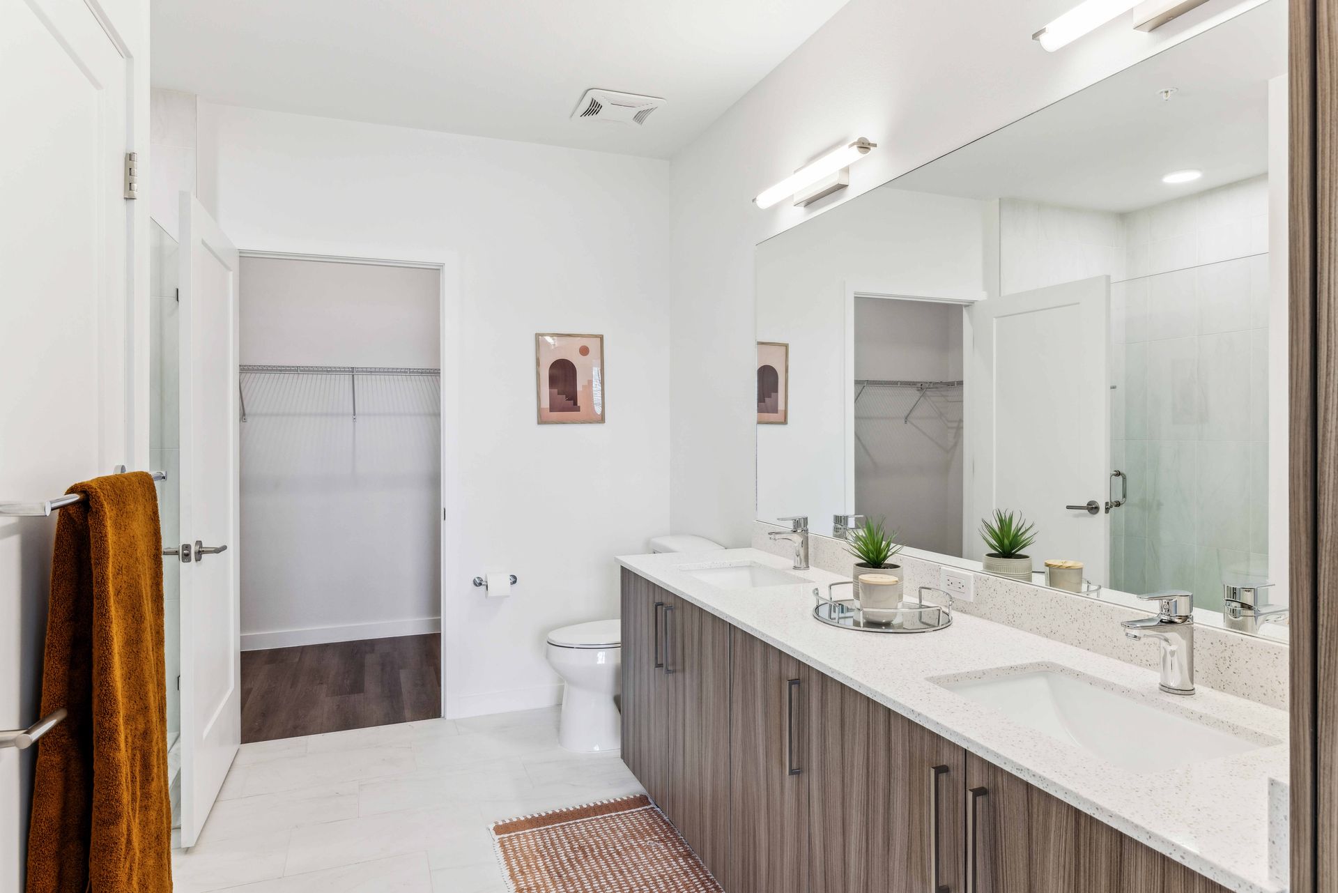 Bathroom with double vanity, white walls, and walk-in closet. Brown towels.