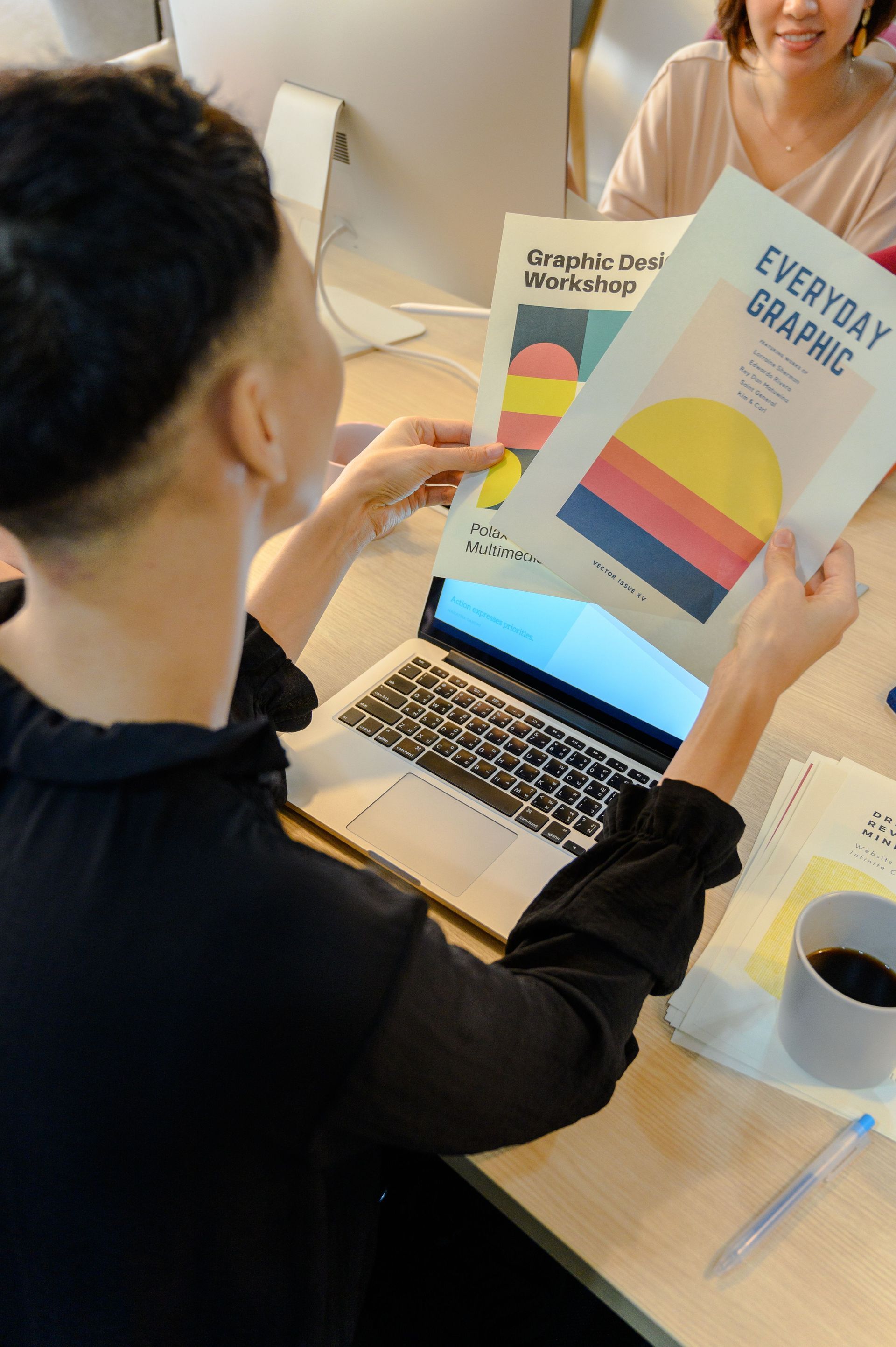Person holding colorful book covers at a desk in a bright office meeting setting