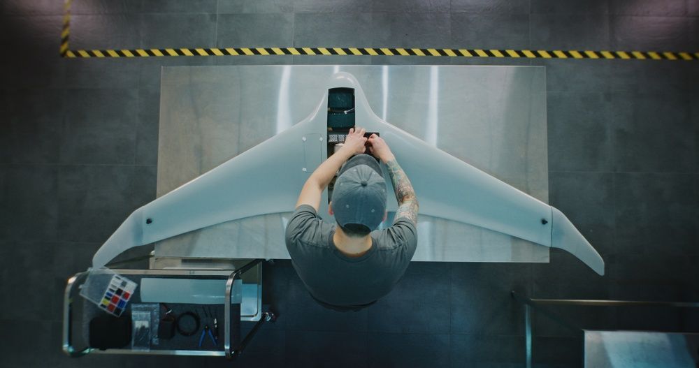 A person working on a large, futuristic-looking drone on a workbench. Overhead shot.