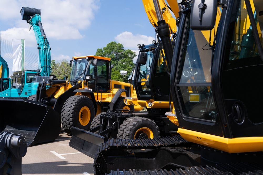 Construction equipment, including excavators and loaders, parked outdoors on a sunny day.