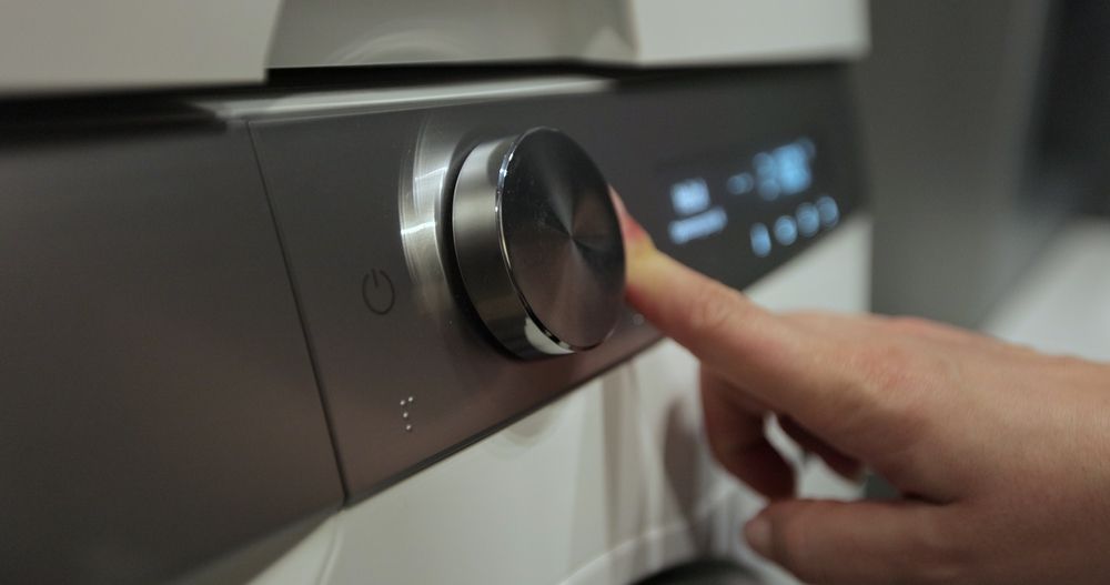 A person's finger turns the circular silver control knob on a modern, dark-toned appliance control panel.