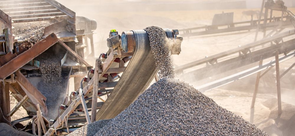 Conveyor belt in a quarry, transporting and depositing gravel onto a large pile, dusty setting.