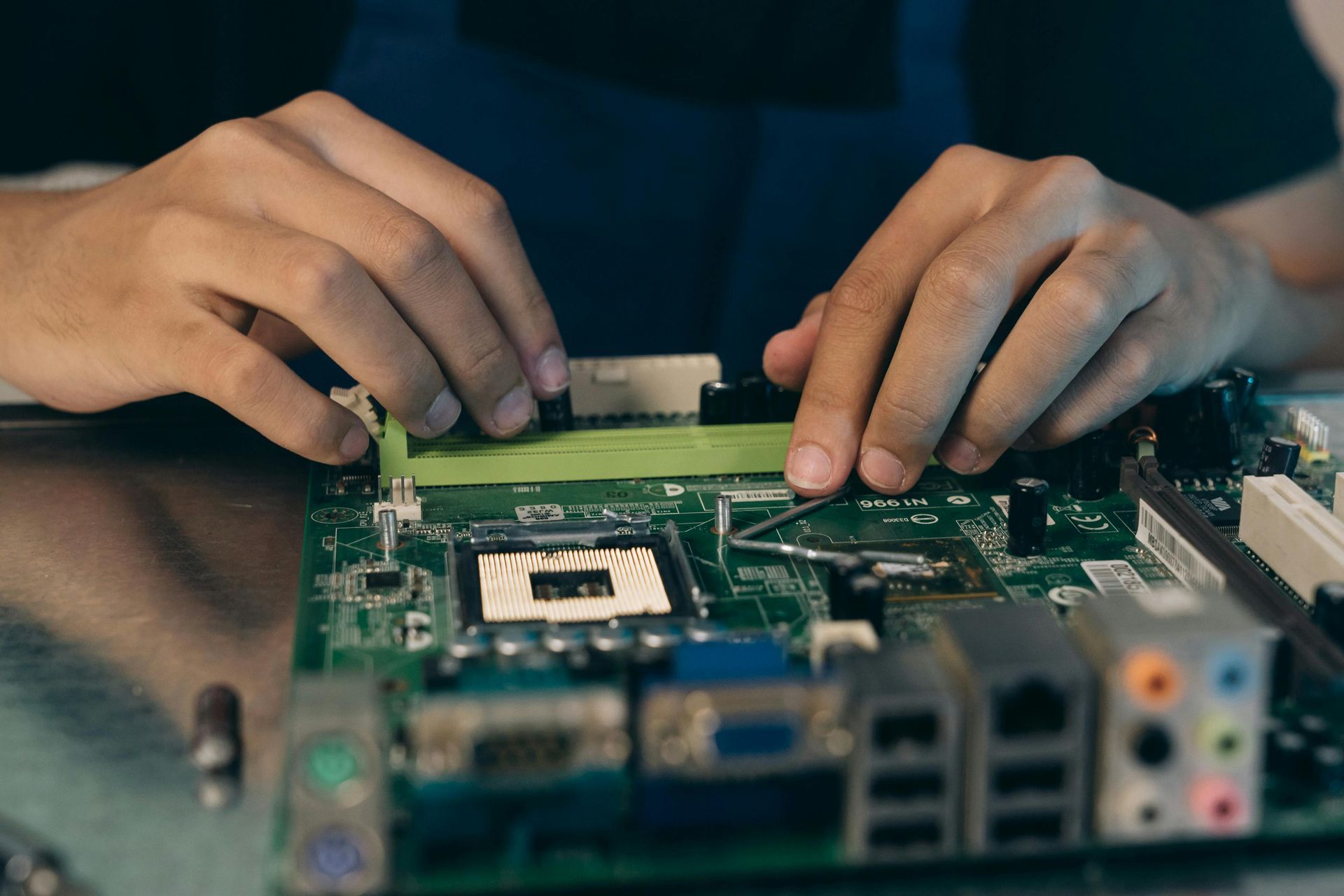 Hands installing a green RAM stick into a computer motherboard.