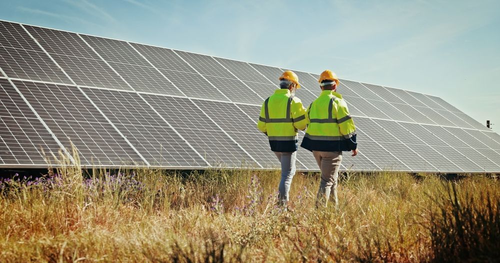 Two people in safety vests and hard hats walk toward solar panels.