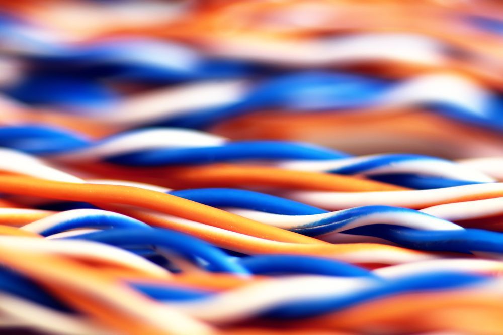 Close-up of twisted blue, white, and orange electrical wires, out of focus in the background.