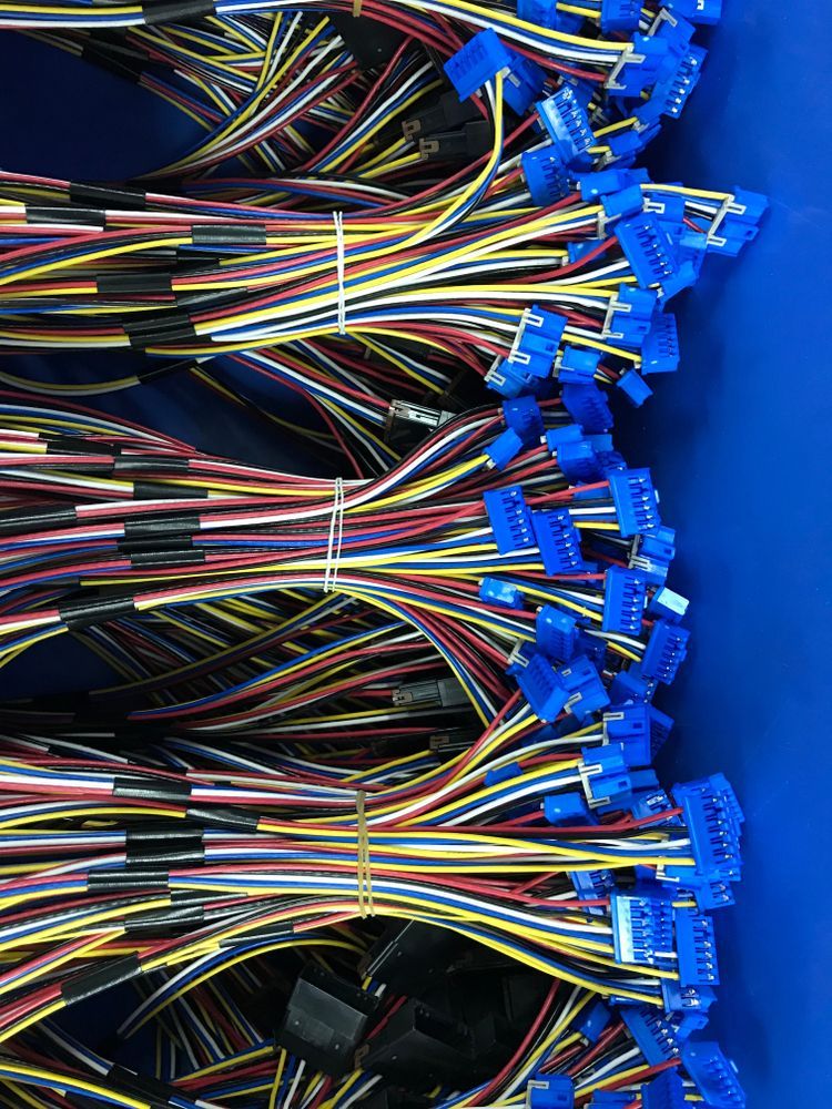 Person operating a tensile testing machine; a white cable is being tested in a lab setting.
