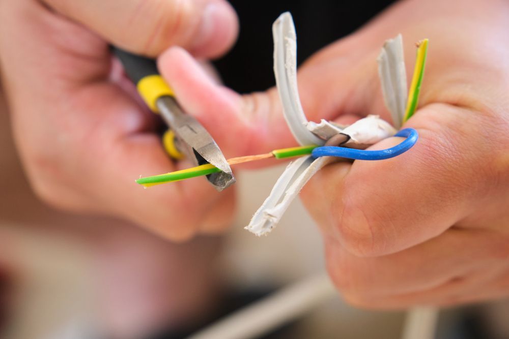 Hands cutting electrical wires with pliers.