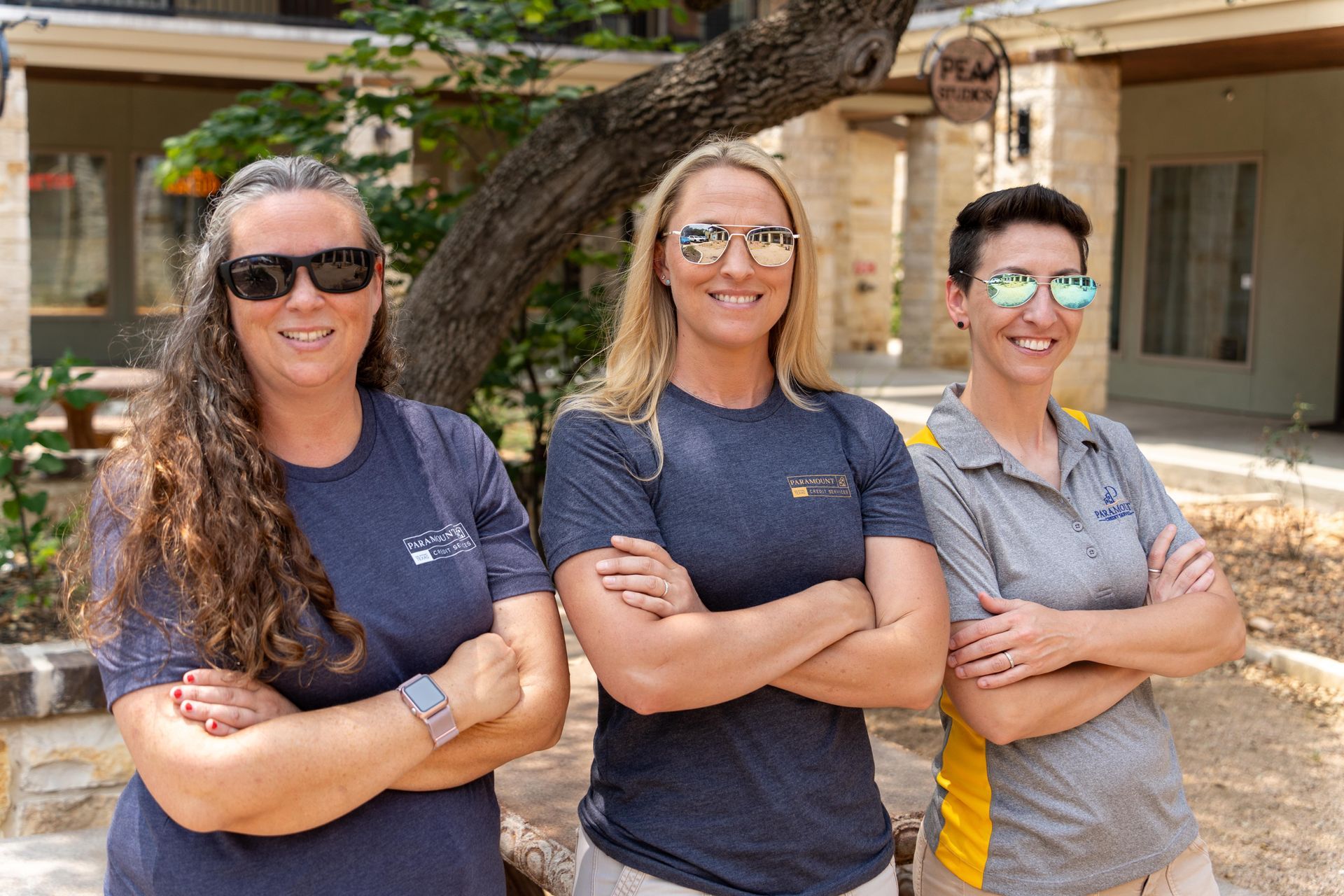 Three women are standing next to each other with their arms crossed in front of a house.