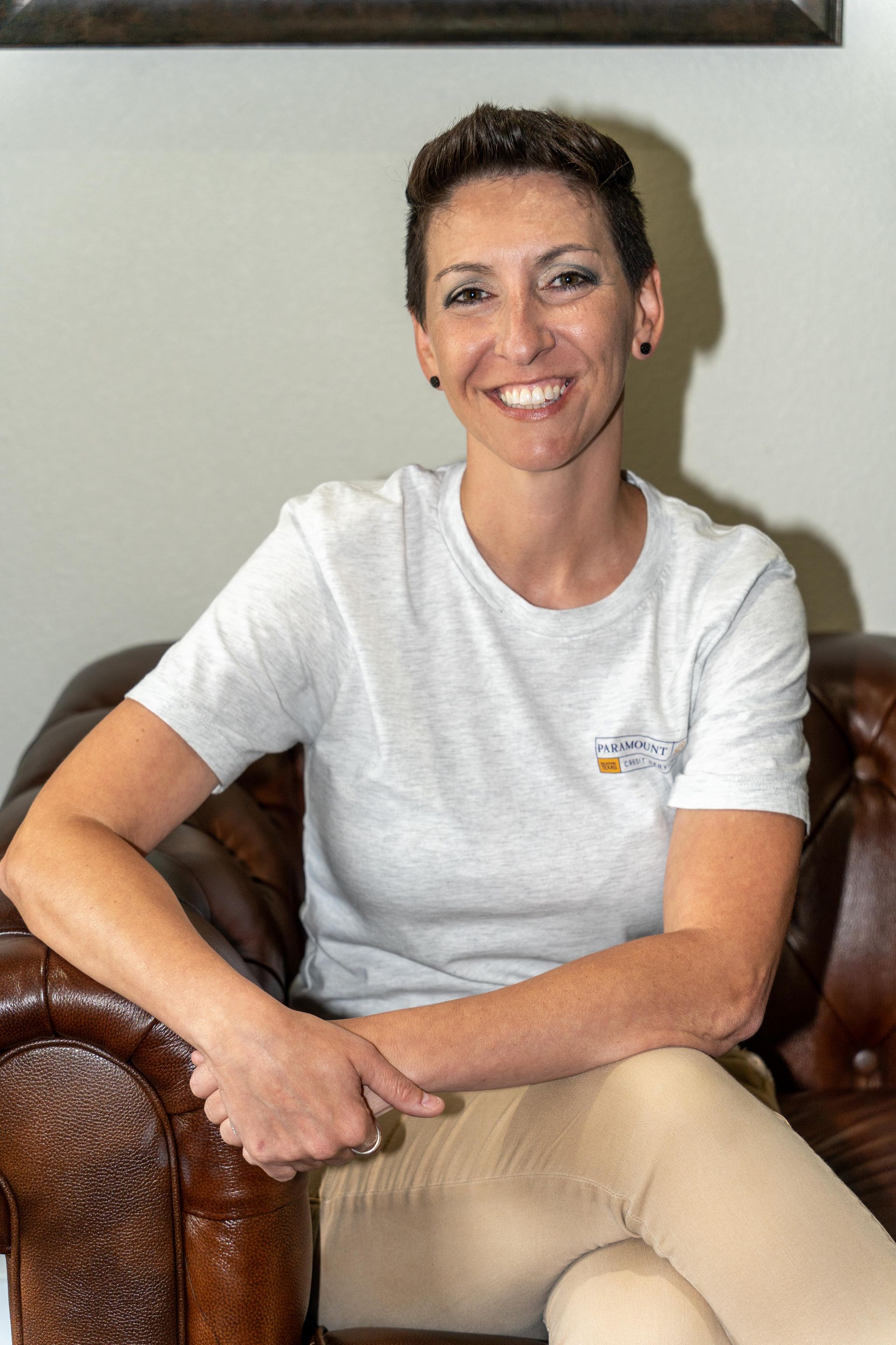 A woman is sitting in a chair with her legs crossed and smiling.