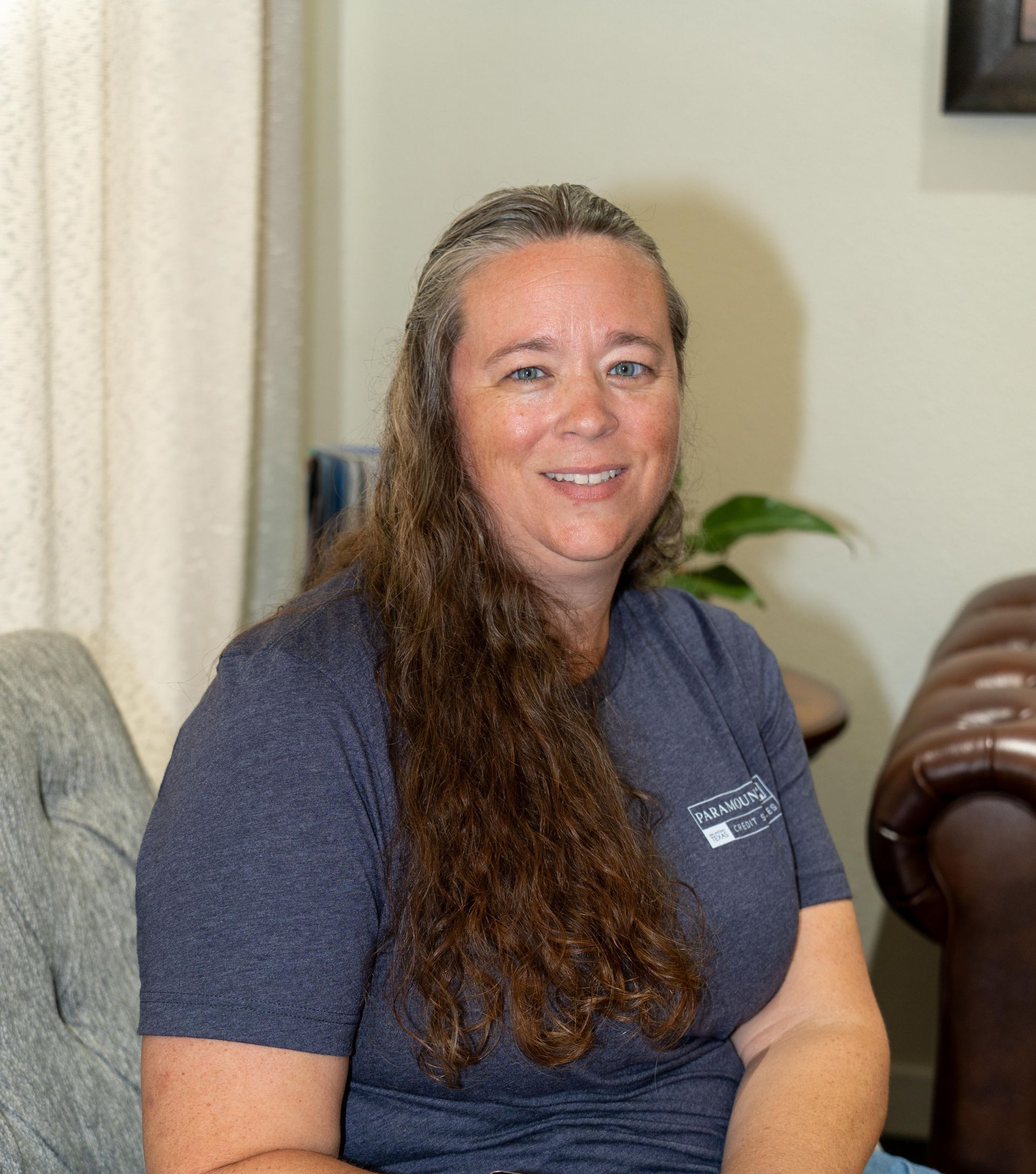 A woman is sitting on a couch in a living room smiling.