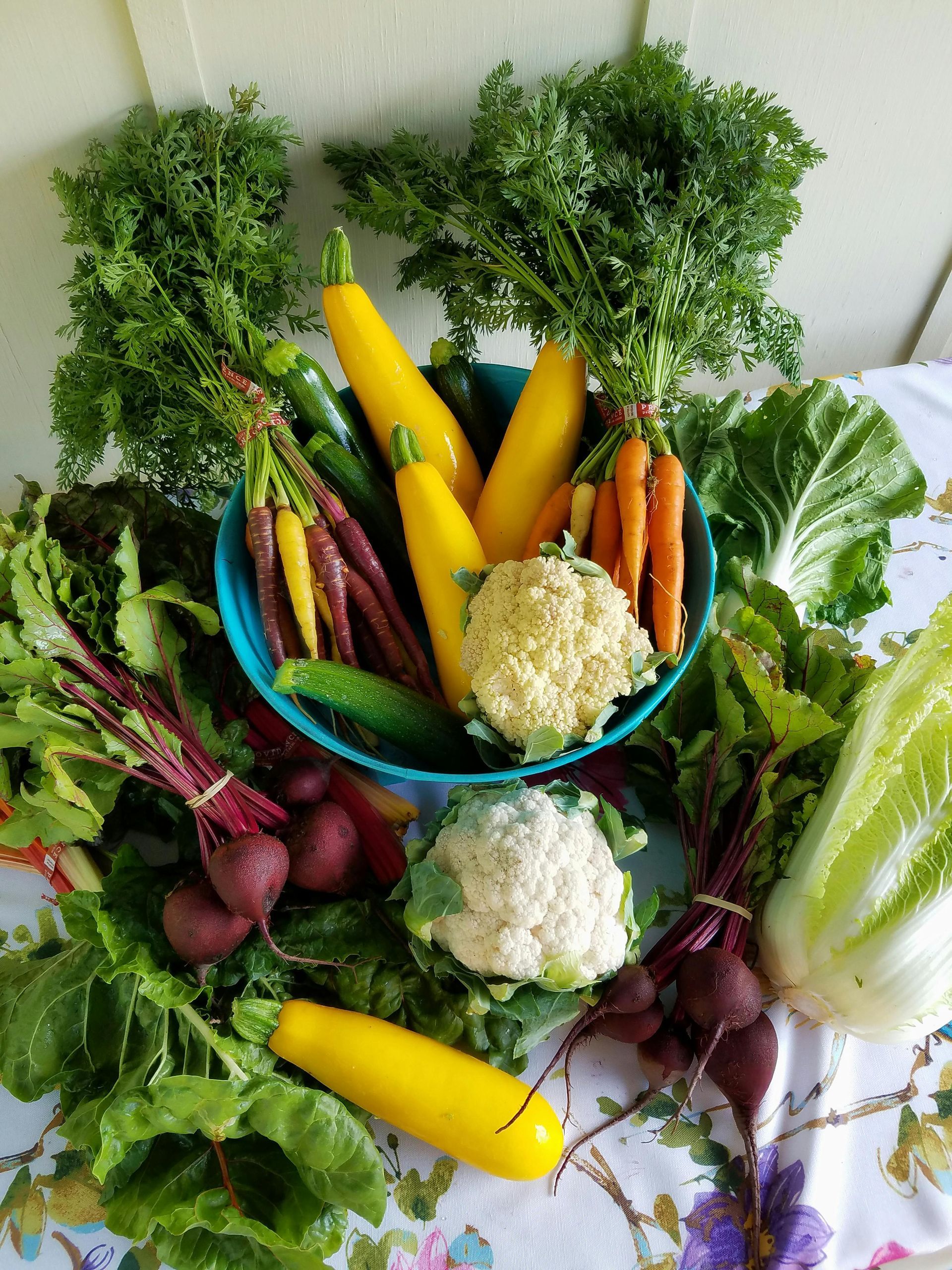 A bowl of vegetables is sitting on a table surrounded by other vegetables.