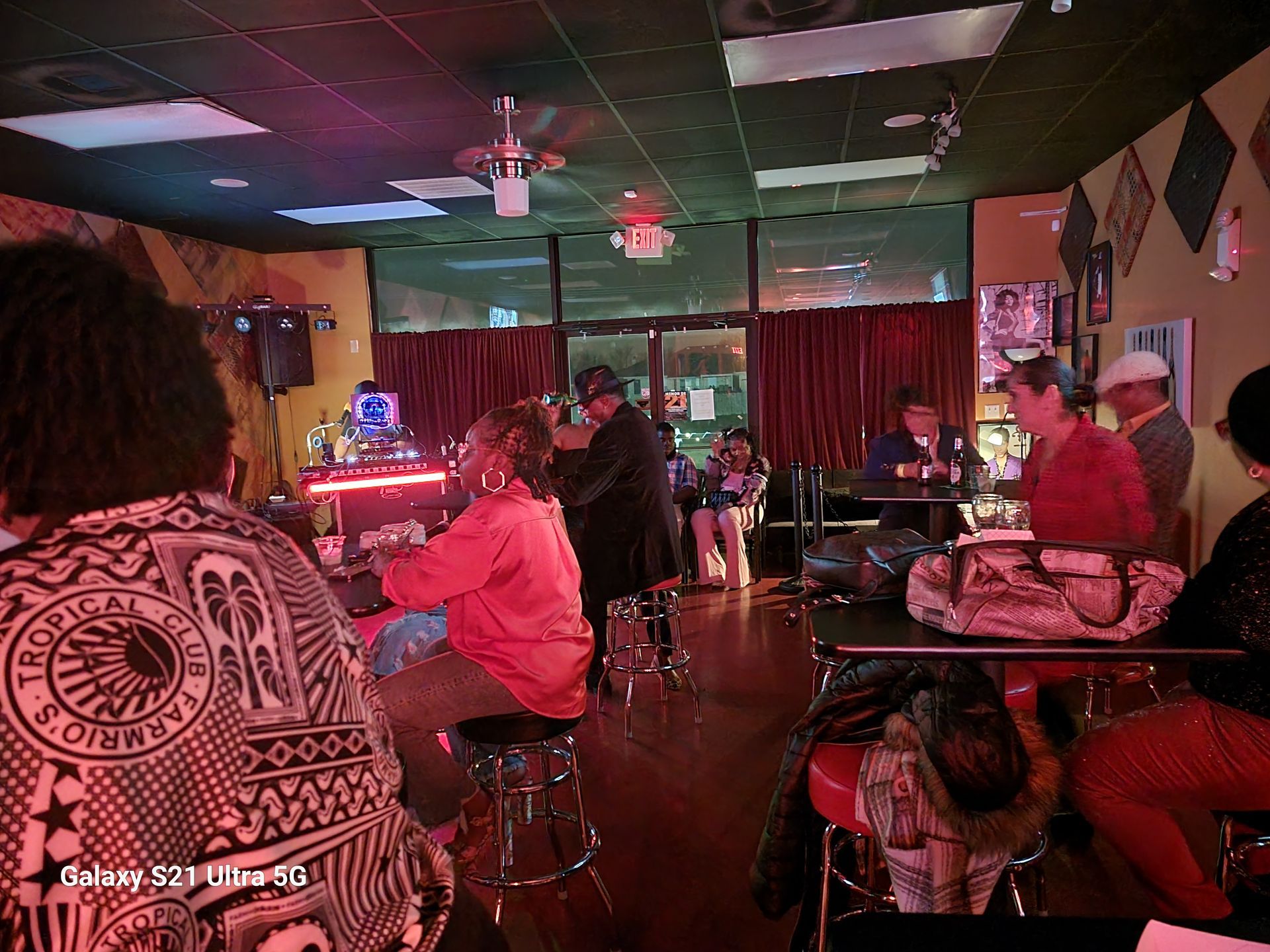 People at a jazz bar: musicians on stage, patrons at tables, red lighting.