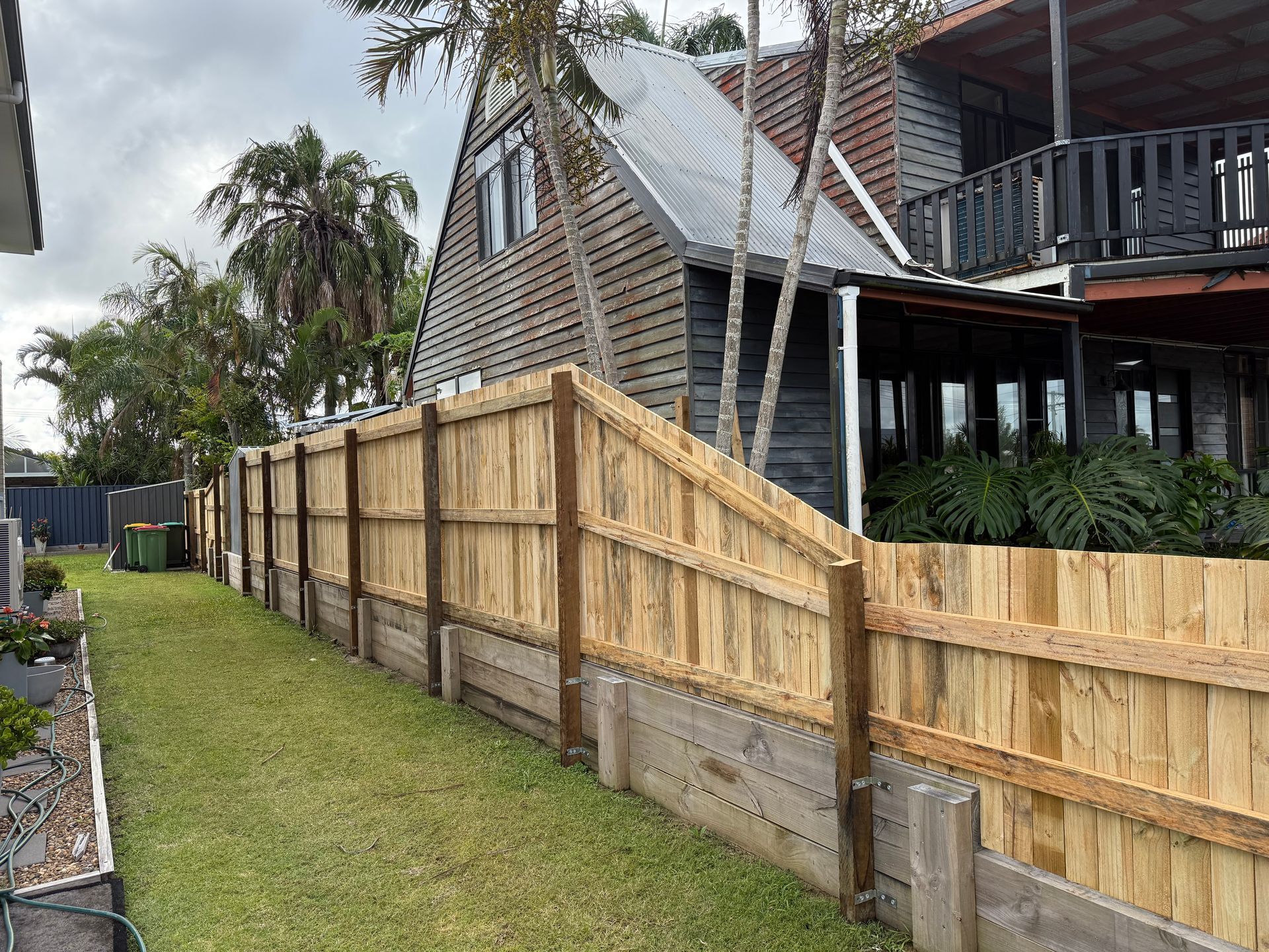 A wooden fence surrounds a lush green yard in front of a house.