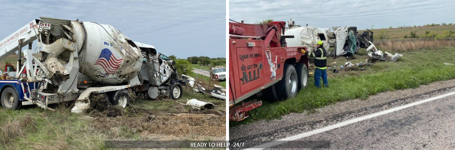 Overturned cement truck beside red tow truck on a grassy roadside, with debris scattered nearby.