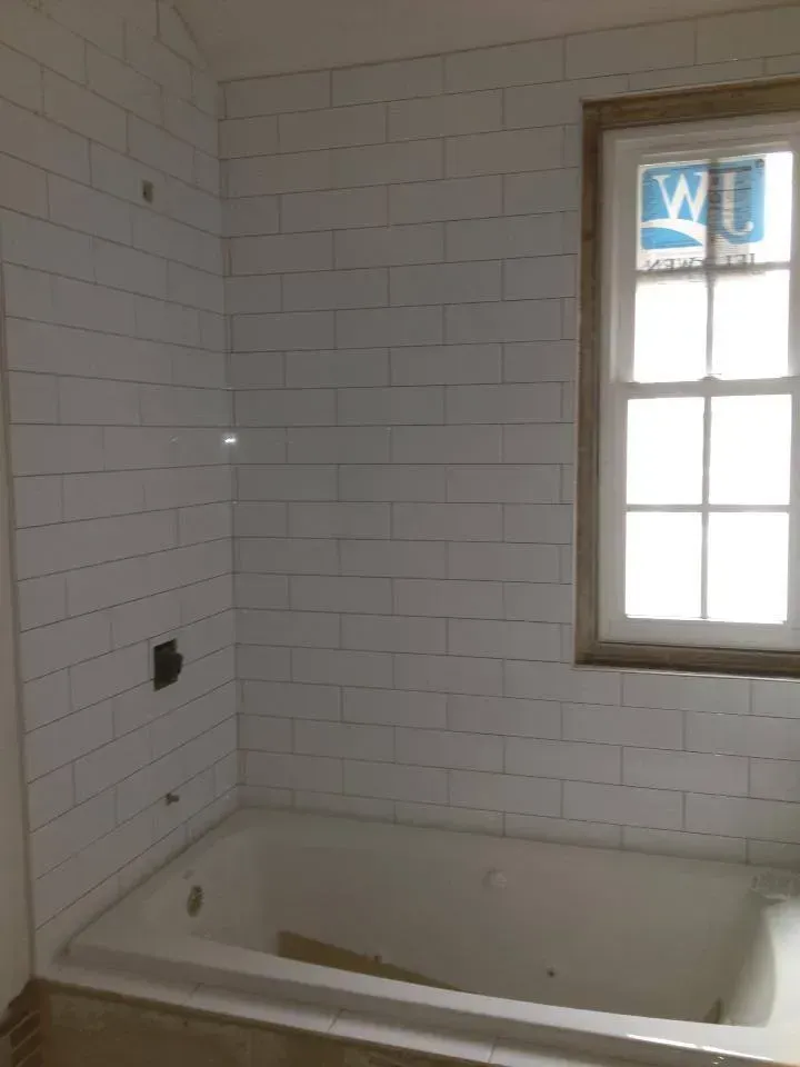 A bathtub in a bathroom with white tiles and a window.