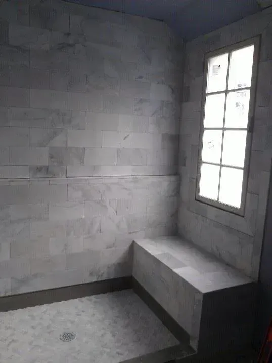 A bathroom with a window and a bench in the shower.
