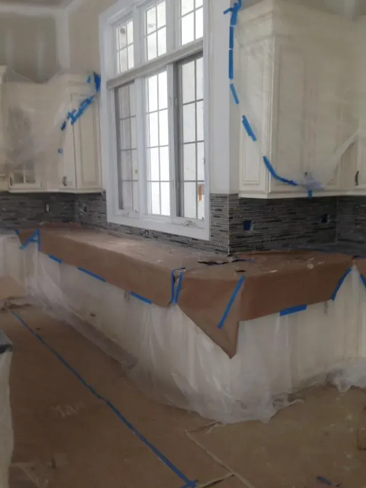 A kitchen with white cabinets and a large window is being painted.