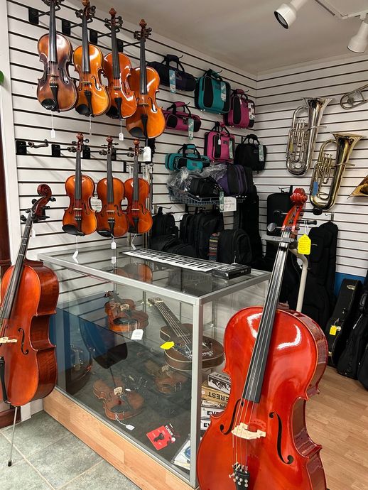 Violin shop interior with violins, cellos, cases, and accessories on display.