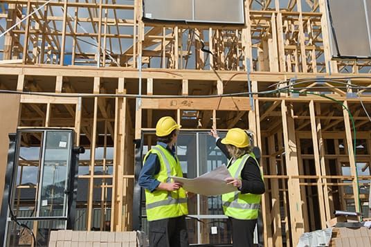 Two construction workers are standing in front of a building under construction.