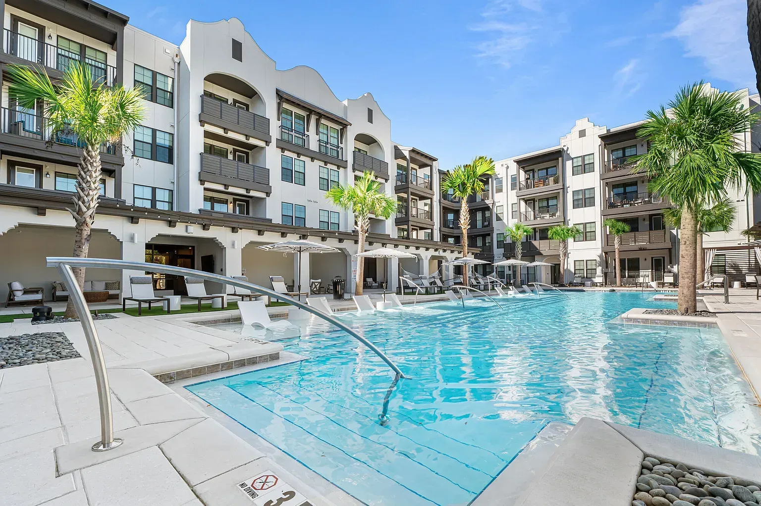 Outdoor pool at an apartment community with lounge chairs and palm trees.