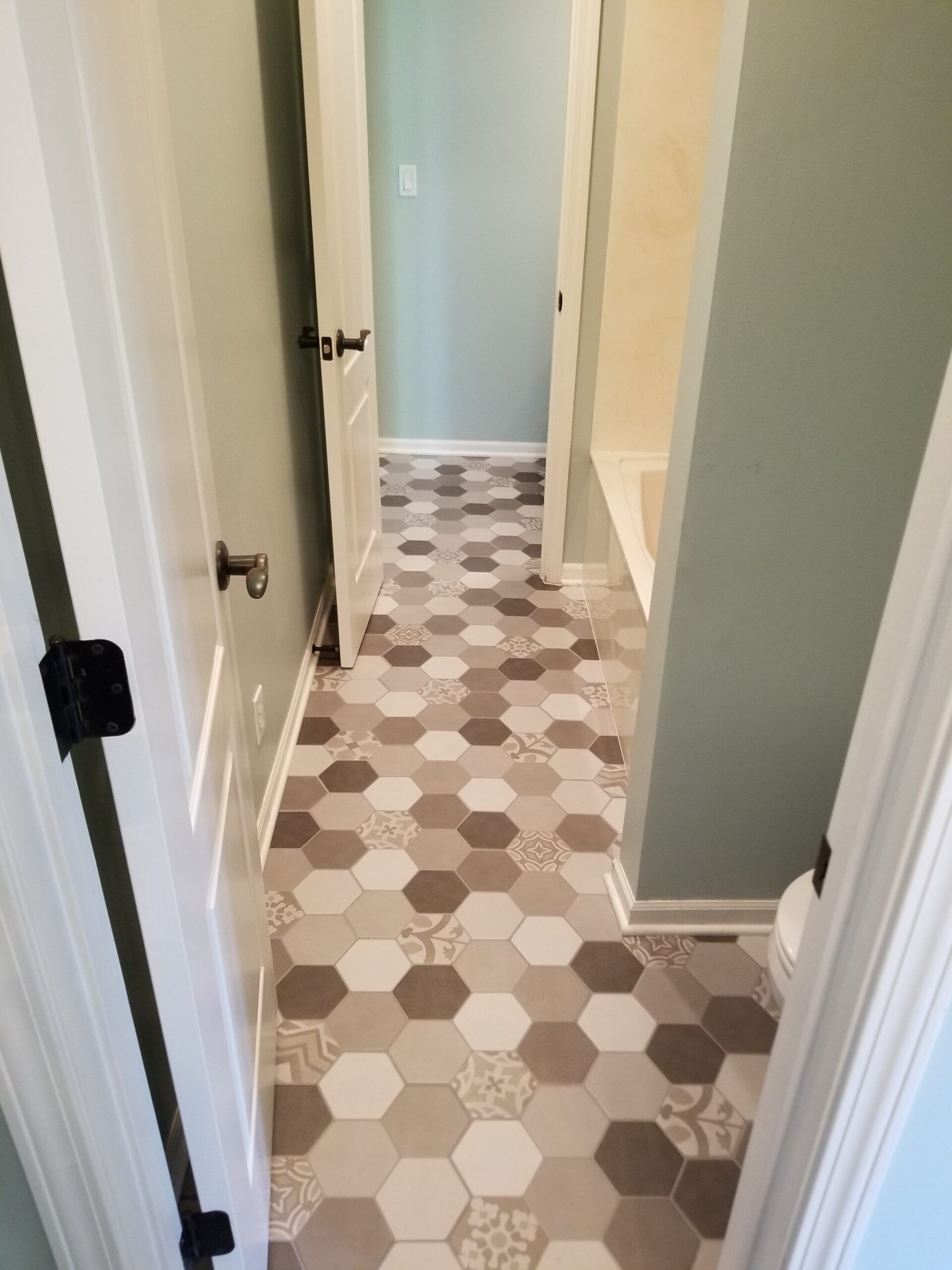 A hallway with hexagonal tiles on the floor leading to a bathroom.