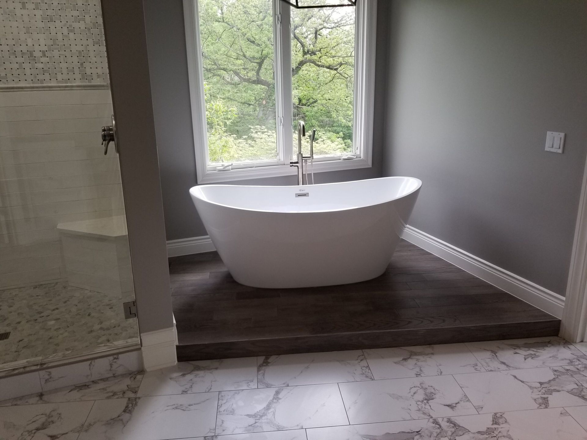 A bathtub is sitting on a marble floor in a bathroom next to a window.
